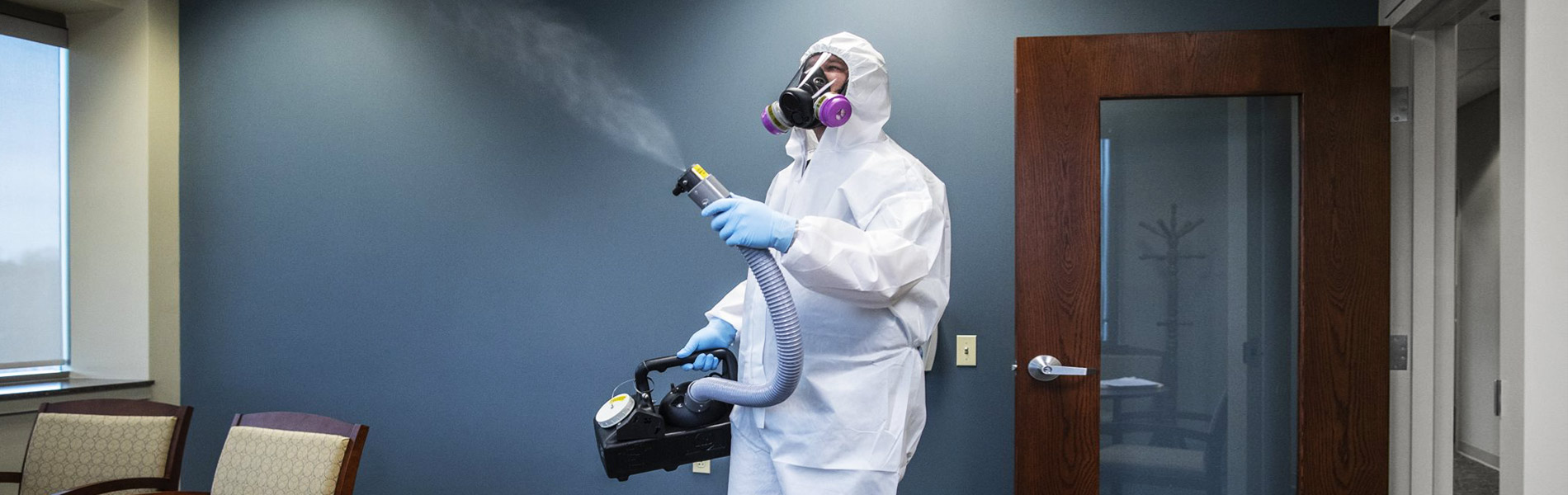 Man with protective suit spraying house